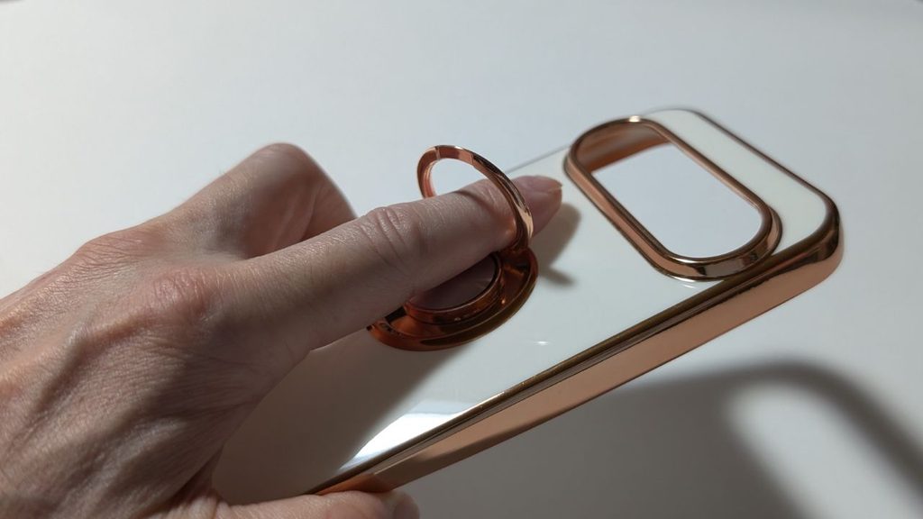 白とピンクゴールドのスマホケースを手で持ち、背面リングに指を通した状態を撮影した写真